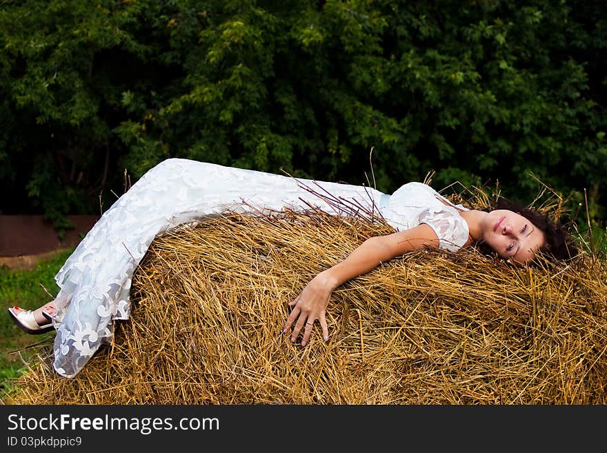 Brunette woman in white dress on hay in the woods