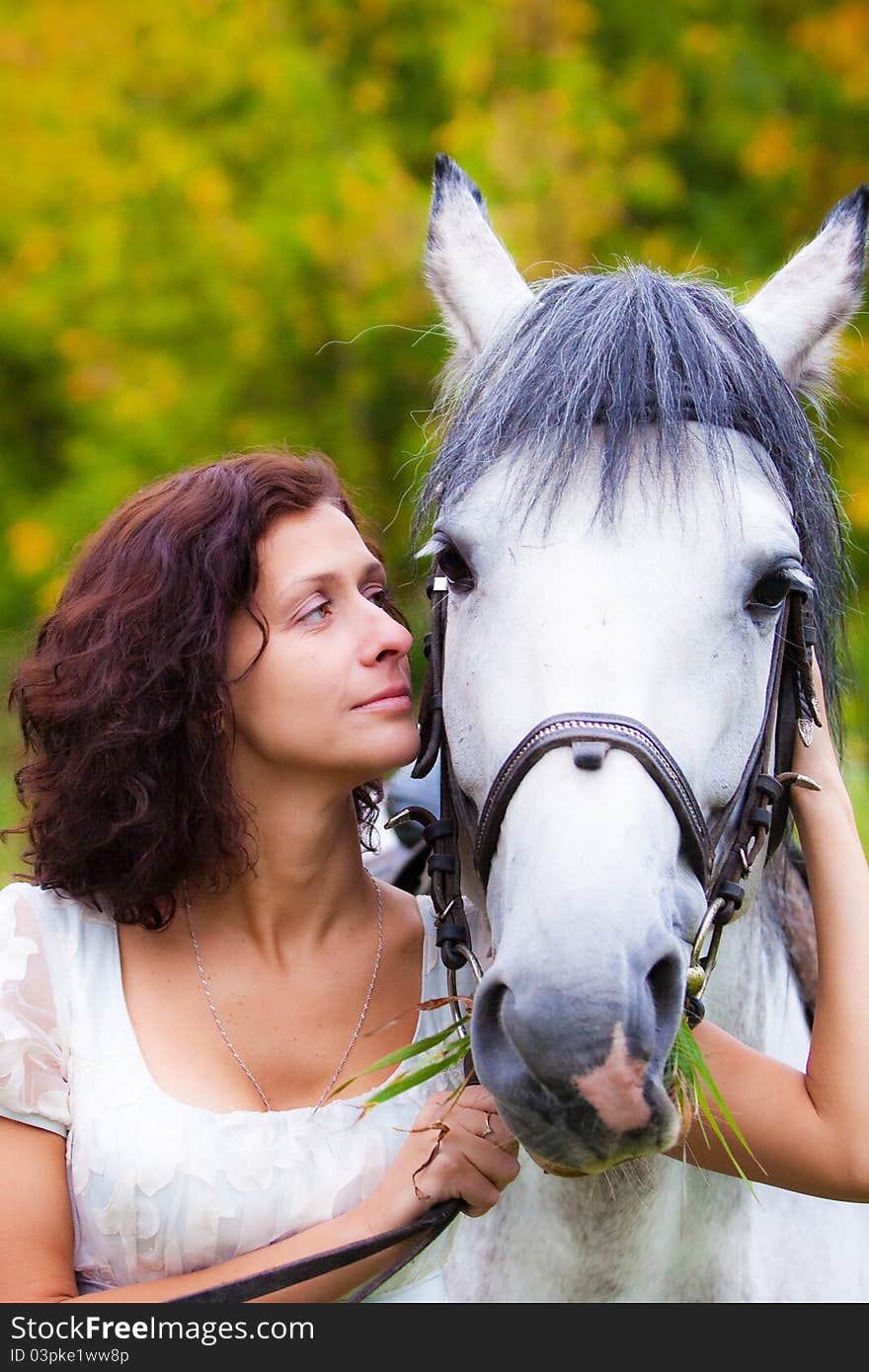 Beautiful woman in white with a horse in the park