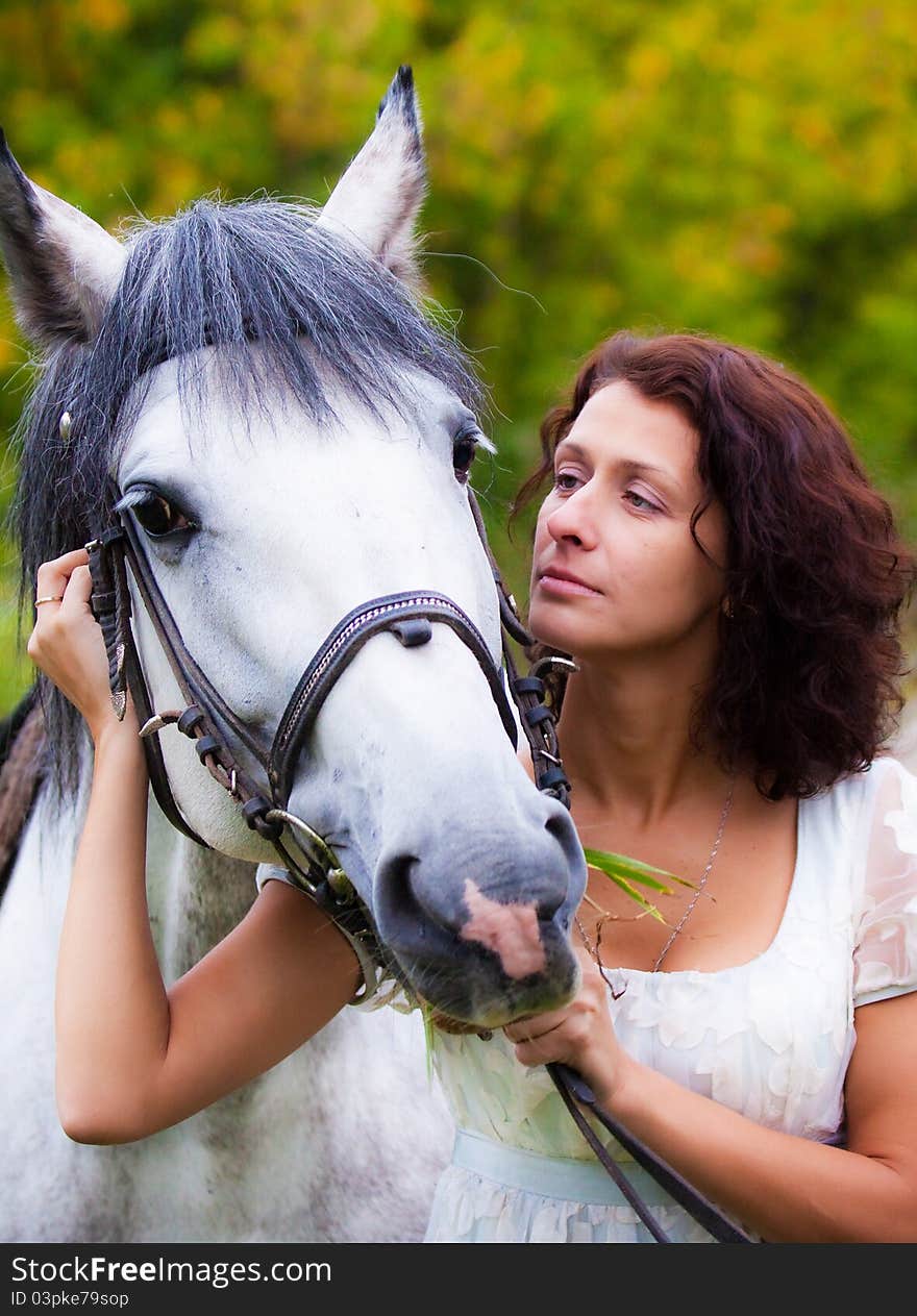 Beautiful woman in white with a horse in the park