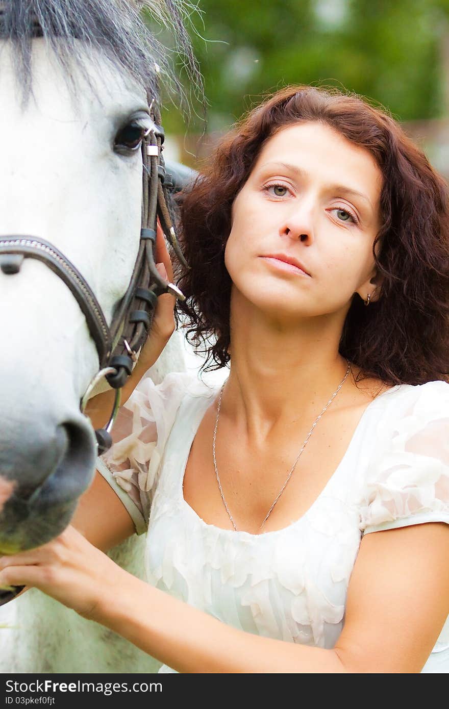 Beautiful woman in white with a horse in the park