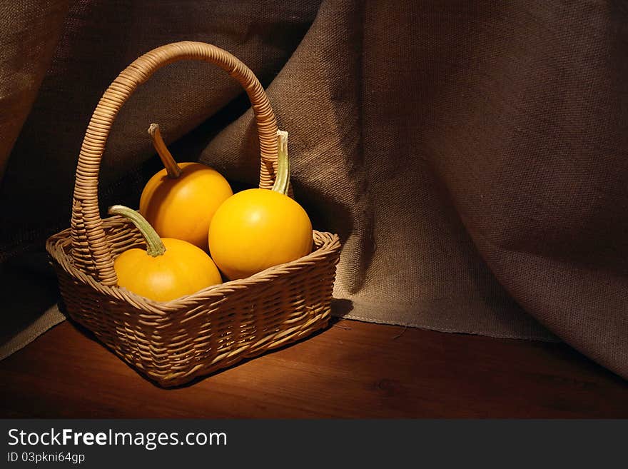 Woven basket with three pumpkins on dark canvas background. Woven basket with three pumpkins on dark canvas background