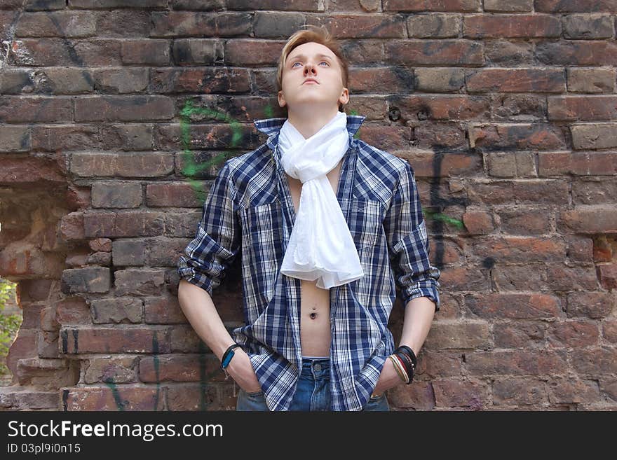 Young man standing near red brick wall. he has white scarf and blue shirt. he is looking up. Young man standing near red brick wall. he has white scarf and blue shirt. he is looking up