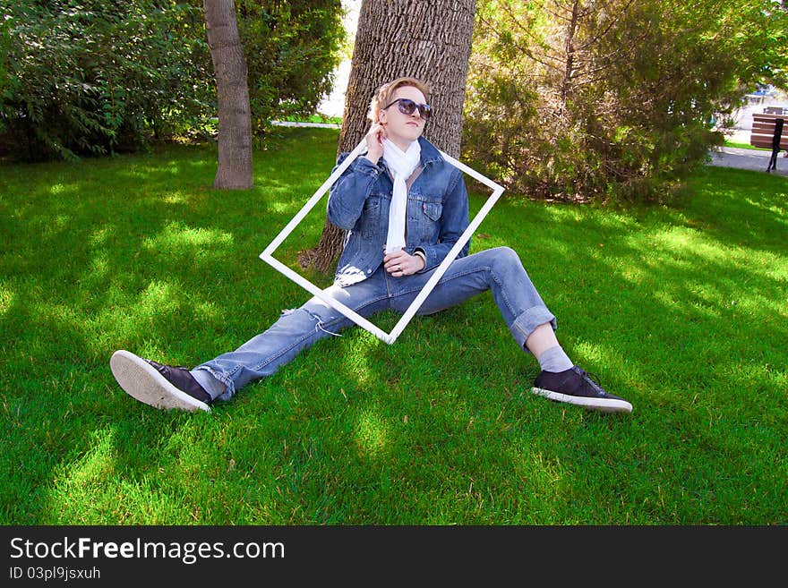 Young human on the green grass with white frame, he has blue goggles, jean jacket and white scarf