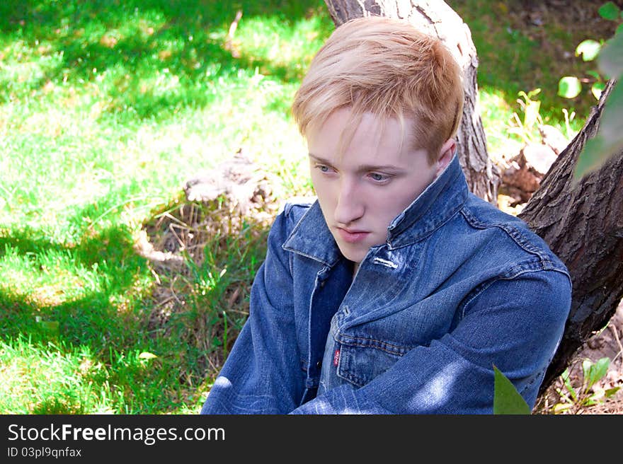 Young human on the green grass , he has jean jacket, he is near of tree