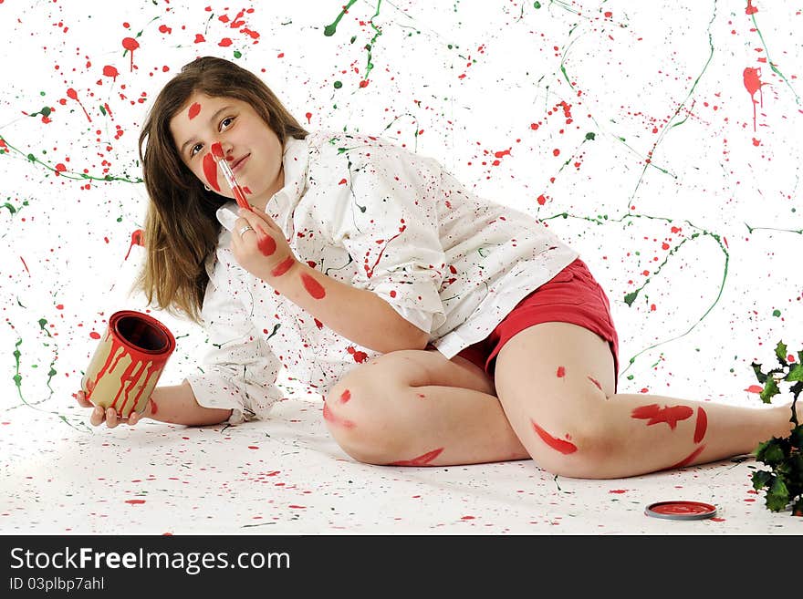 An attractive preteen painting her nose red while surrounded by white splattered with red and green paint. An attractive preteen painting her nose red while surrounded by white splattered with red and green paint.