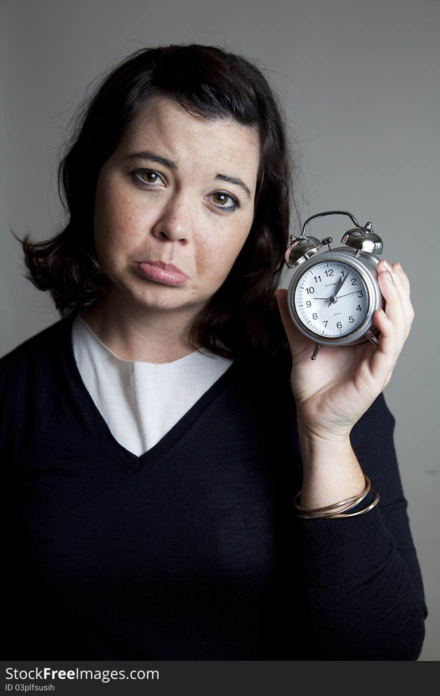 A woman holding a clock with an unhappy expression. A woman holding a clock with an unhappy expression.