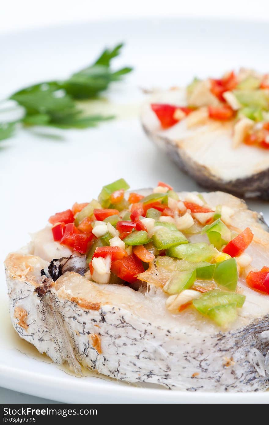 Hake fillets with peppers presented on a white background at lunchtime