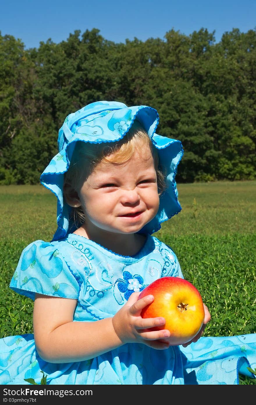 Funny little girl with a big apple in the meadow