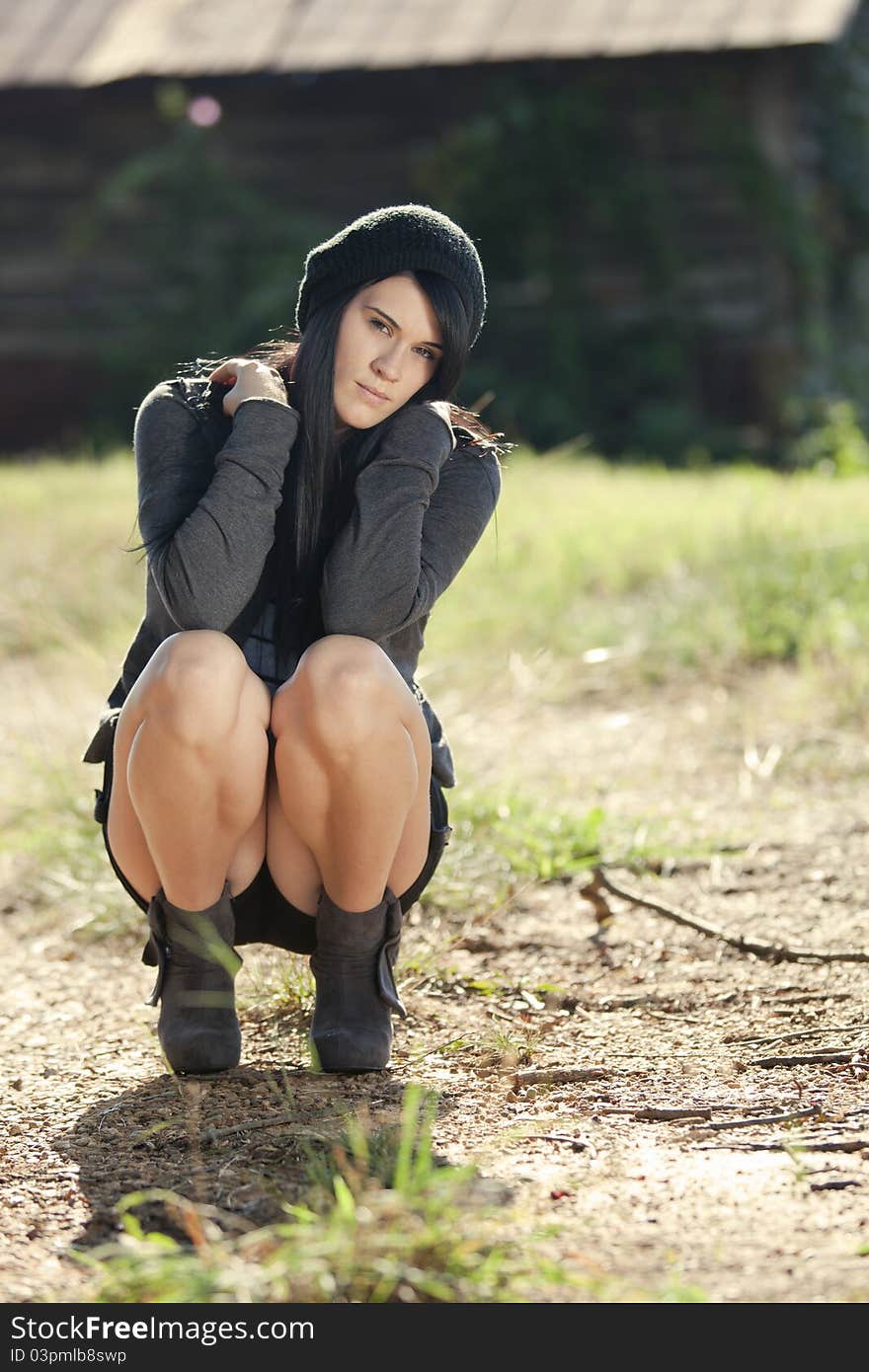 A beautiful young female model crouches oudside near a barn covered in ivy. A beautiful young female model crouches oudside near a barn covered in ivy