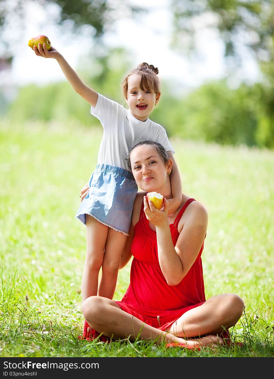 Beautiful young mother and her daughter eating pears in the park on a sunny summer day (focus on the women). Beautiful young mother and her daughter eating pears in the park on a sunny summer day (focus on the women)