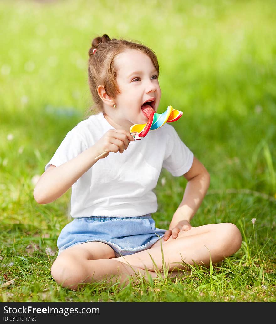 Cute little girl eating a lollipop on the grass in summertime. Cute little girl eating a lollipop on the grass in summertime