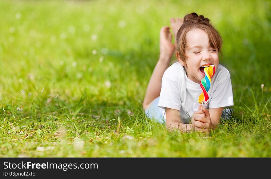 Cute little girl eating a lollipop on the grass in summertime. Cute little girl eating a lollipop on the grass in summertime