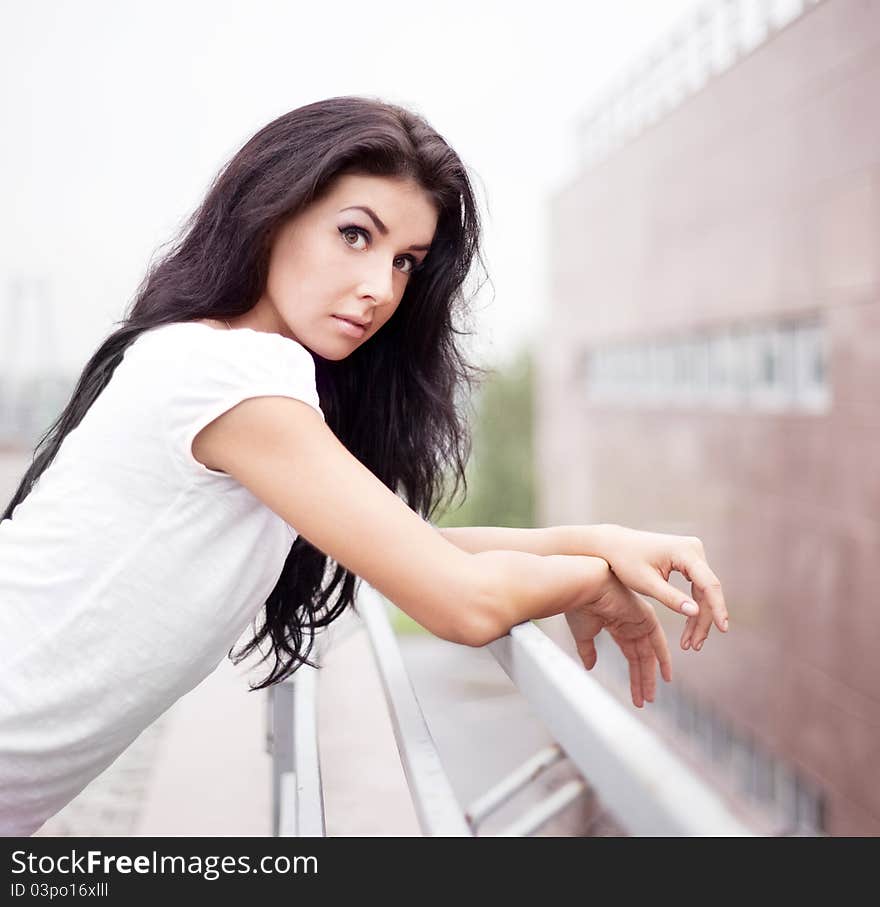 Very beautiful upset young brunette woman near the fence in the street. Very beautiful upset young brunette woman near the fence in the street