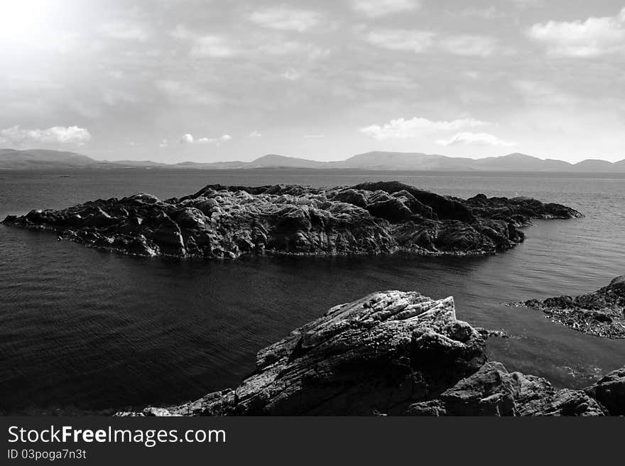 Scenic view in kerry ireland of rocks and sea with mountains against a beautiful cloudy sky in black and white. Scenic view in kerry ireland of rocks and sea with mountains against a beautiful cloudy sky in black and white