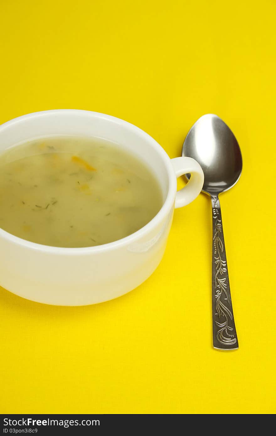 White bowl of soup on a yellow background next to a spoon is. White bowl of soup on a yellow background next to a spoon is