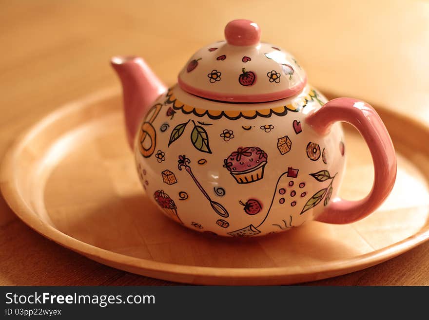 A cute pink teapot on the table with cartoony cupcake design. A cute pink teapot on the table with cartoony cupcake design.