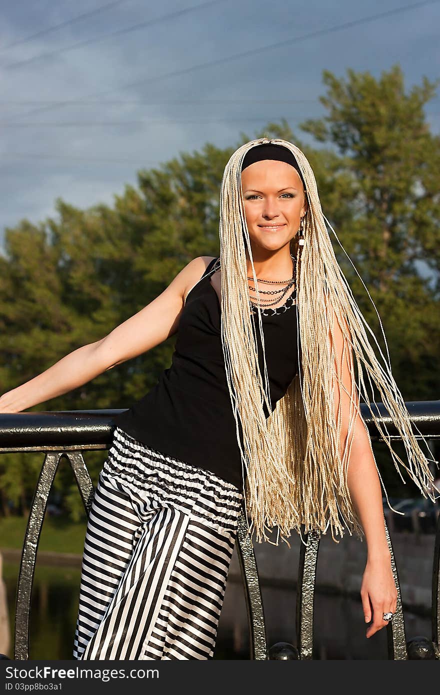 Young woman with braided locks standing on the bridge and smiling