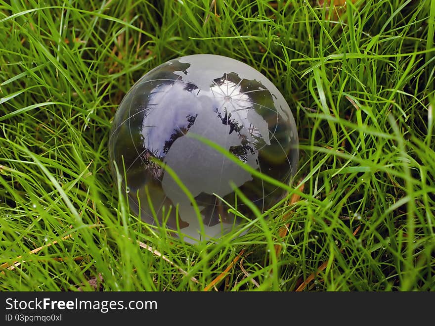 Crystal-clear globe in the green grass as protection and concern of environment