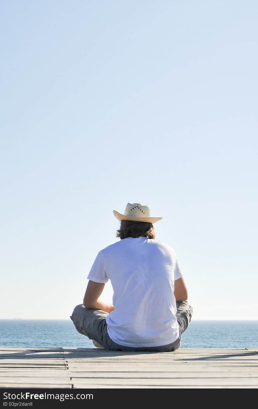 Young man sitting on the beach in straw hat. Young man sitting on the beach in straw hat