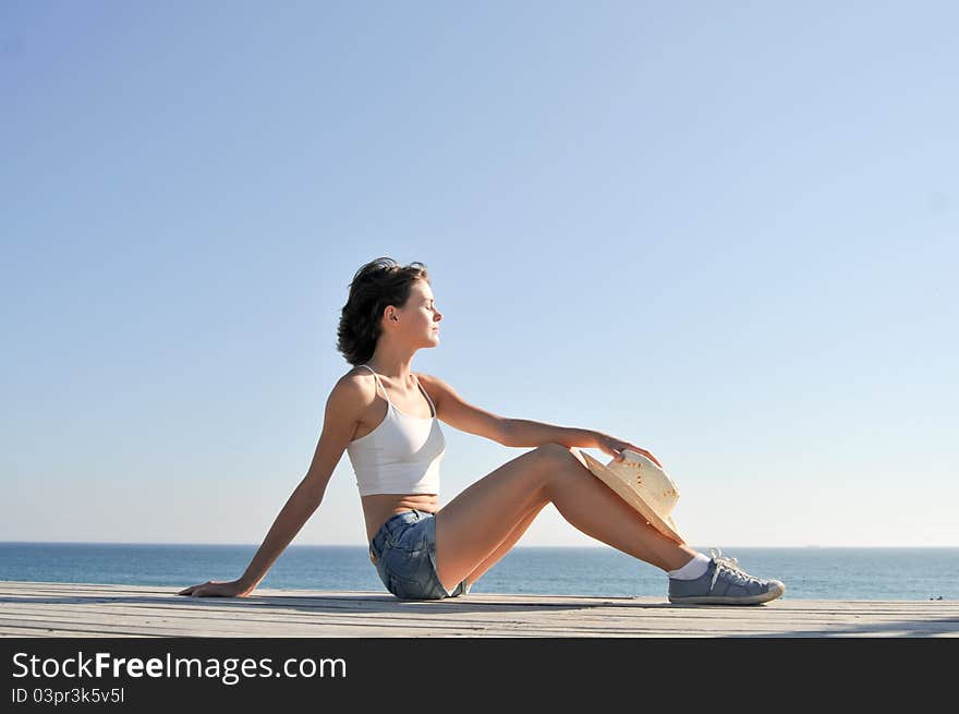 Young woman sitting on the beach in straw hat. Young woman sitting on the beach in straw hat