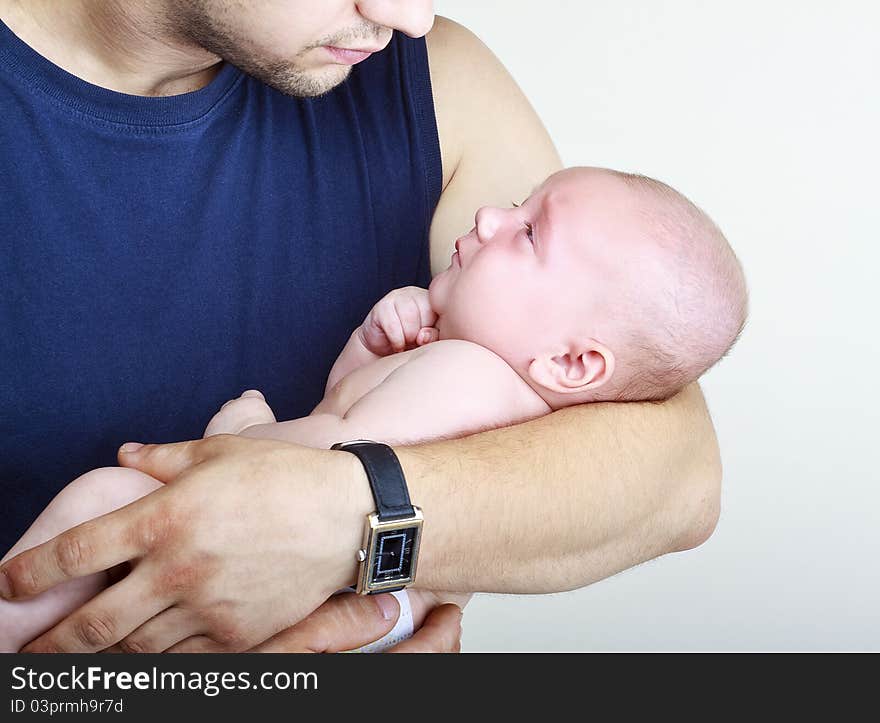 A good father holding his son in his arms and looks at it on a light background