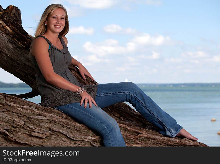 Beautiful young blond model posing on tree by lake. Beautiful young blond model posing on tree by lake