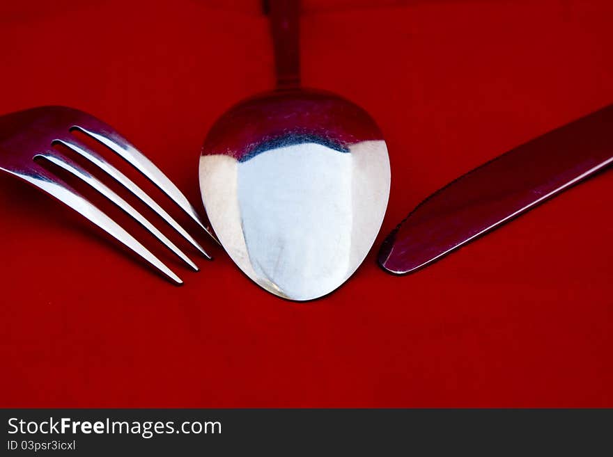 A cutlery set of a spoon, a fork, and a knife on red background. A cutlery set of a spoon, a fork, and a knife on red background