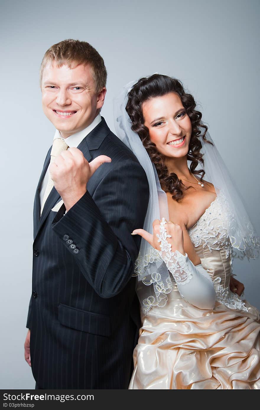 Studio portrait of young beautiful happy just married bride and groom gesticulating on gray background. Studio portrait of young beautiful happy just married bride and groom gesticulating on gray background