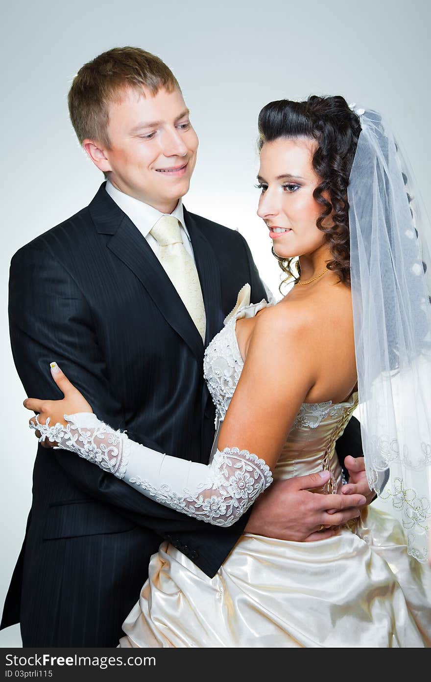 Studio portrait of young beautiful happy just married bride and groom embracing on blue background