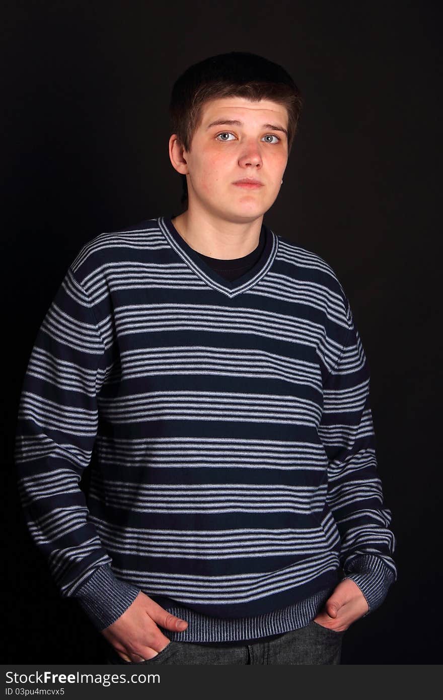 A young boy with his hands in pockets on the black background