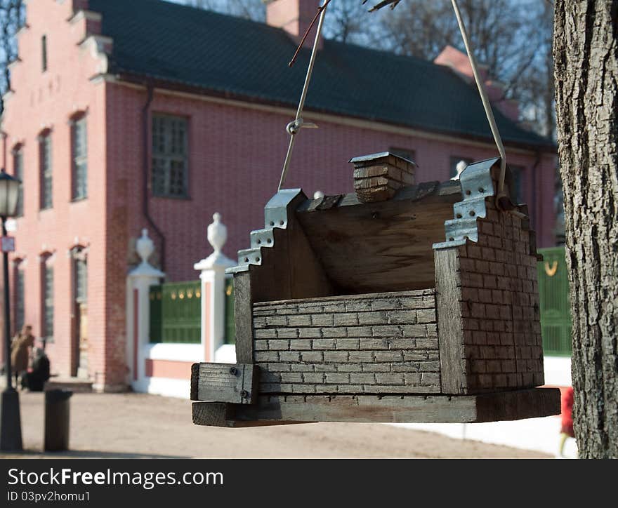 Wooden bird feeder hanging from a tree on a background of brick buildings of the eighteenth century in the park Kuskovo Moscow. Wooden bird feeder hanging from a tree on a background of brick buildings of the eighteenth century in the park Kuskovo Moscow