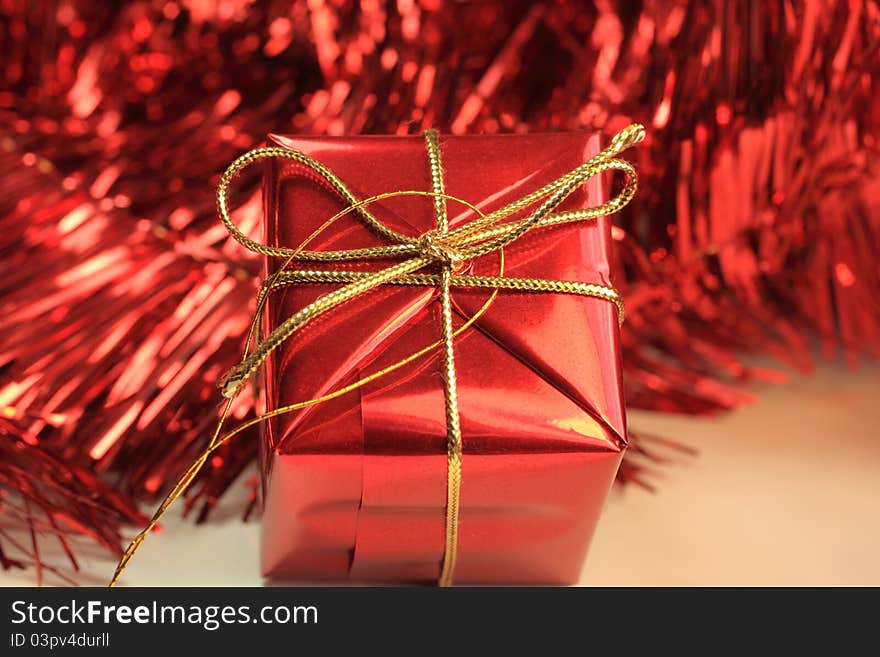 A single Christmas gift in red with gold string bows set against red tinsel.