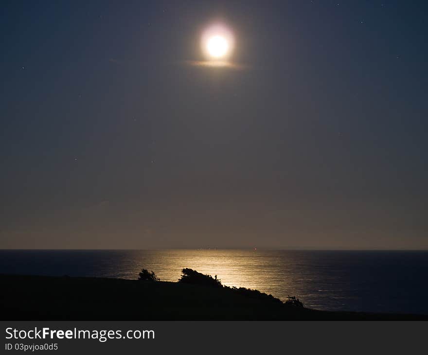 Full bright moon over the sea ocean with far away lights in the background. Full bright moon over the sea ocean with far away lights in the background