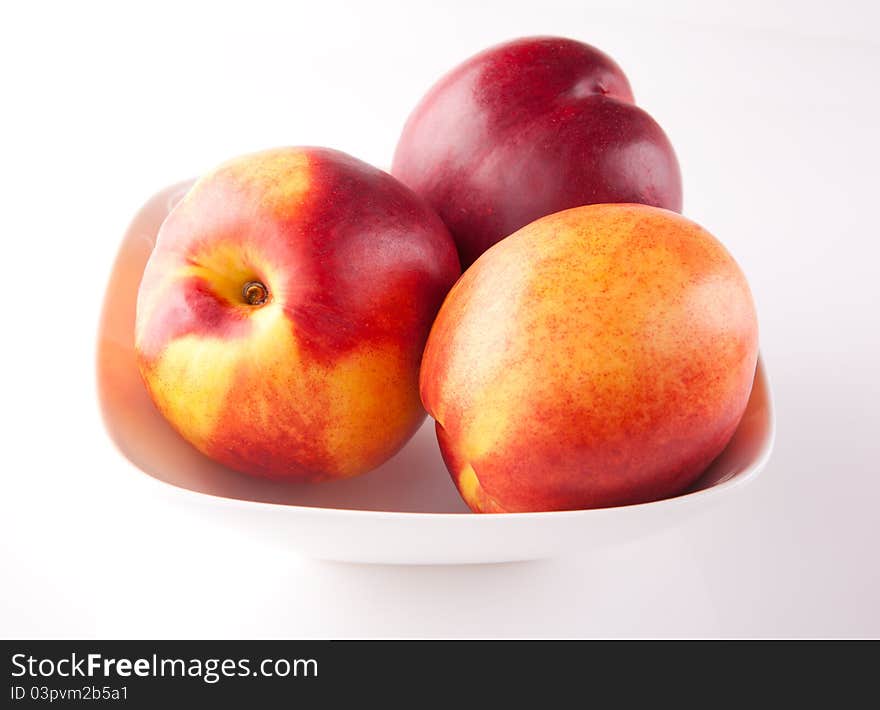 Three fresh peaches on white ceramic plate. Three fresh peaches on white ceramic plate