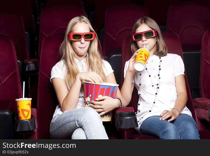 Two girls look three-dimensional cinema, sitting in the glasses, eat popcorn, drink drink. Two girls look three-dimensional cinema, sitting in the glasses, eat popcorn, drink drink