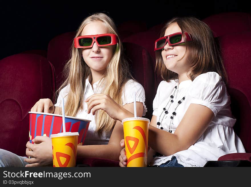 Two girls look three-dimensional cinema, sitting in the glasses, eat popcorn, drink drink. Two girls look three-dimensional cinema, sitting in the glasses, eat popcorn, drink drink