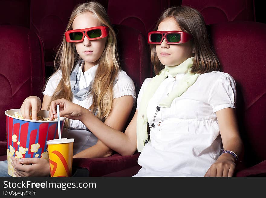 Two girls look three-dimensional cinema, sitting in the glasses, eat popcorn, drink drink. Two girls look three-dimensional cinema, sitting in the glasses, eat popcorn, drink drink