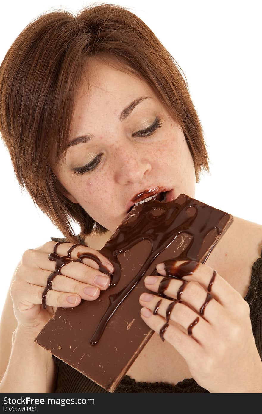 A woman taking a big bite of a chocolate candy bar with chocolate all over her hands. A woman taking a big bite of a chocolate candy bar with chocolate all over her hands.