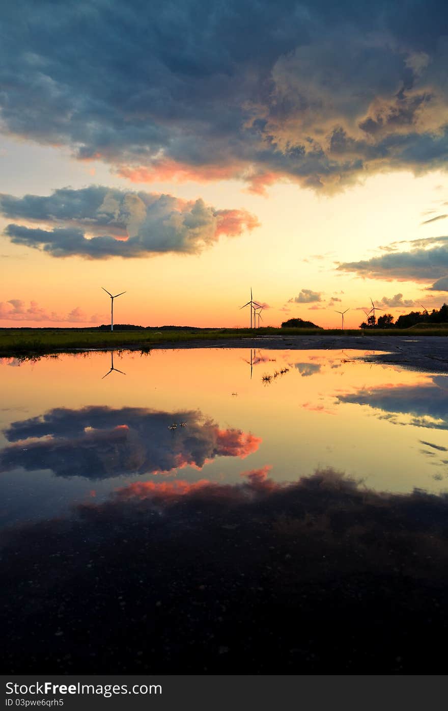 An image of wind turbines reflection in the water at the sunset