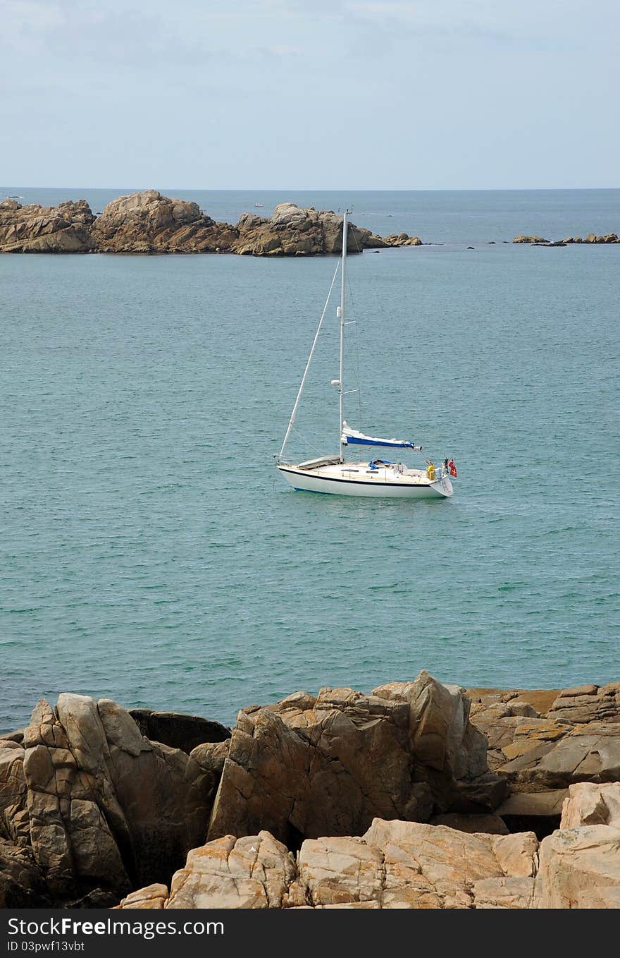 A yacht at anchor in a rocky bay. Blue sea and bold rocks. Guernsey, Channel Islands. A yacht at anchor in a rocky bay. Blue sea and bold rocks. Guernsey, Channel Islands.