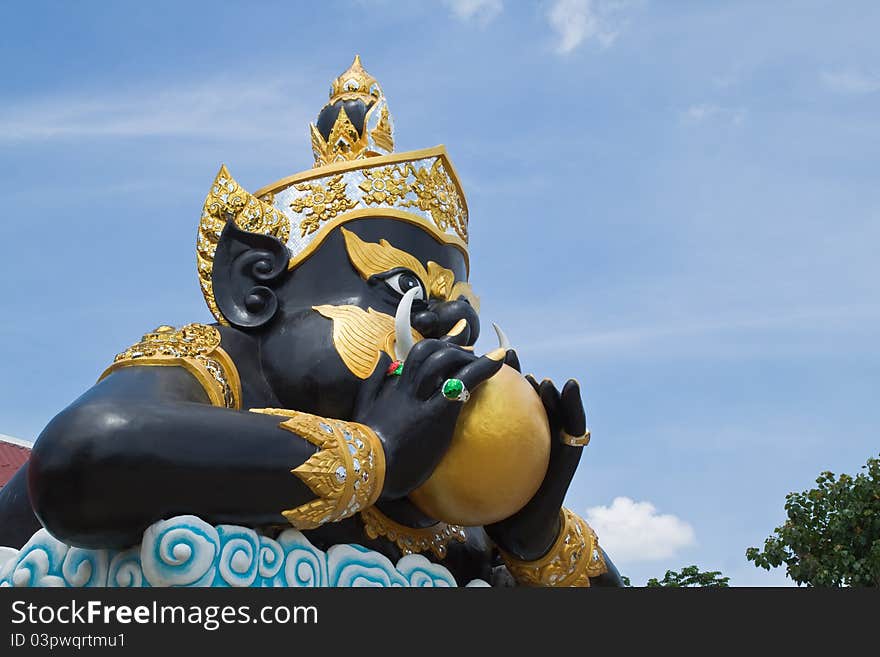 Statue of black deity called Rahu and blue sky background.