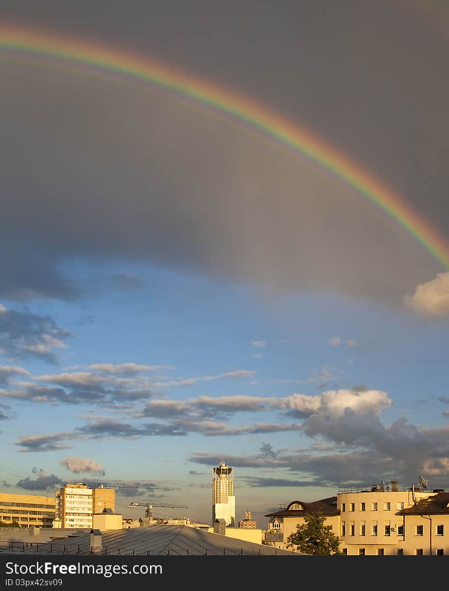 Rainbow on cloudy sky over city roofs