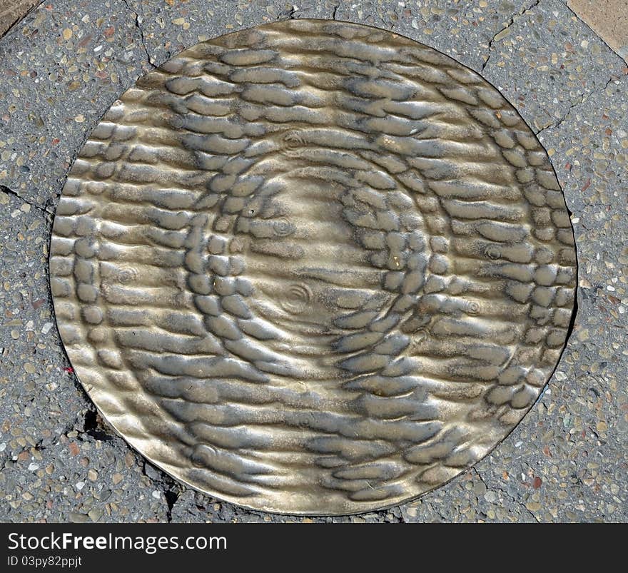 Grunge brass manhole cover on pavement