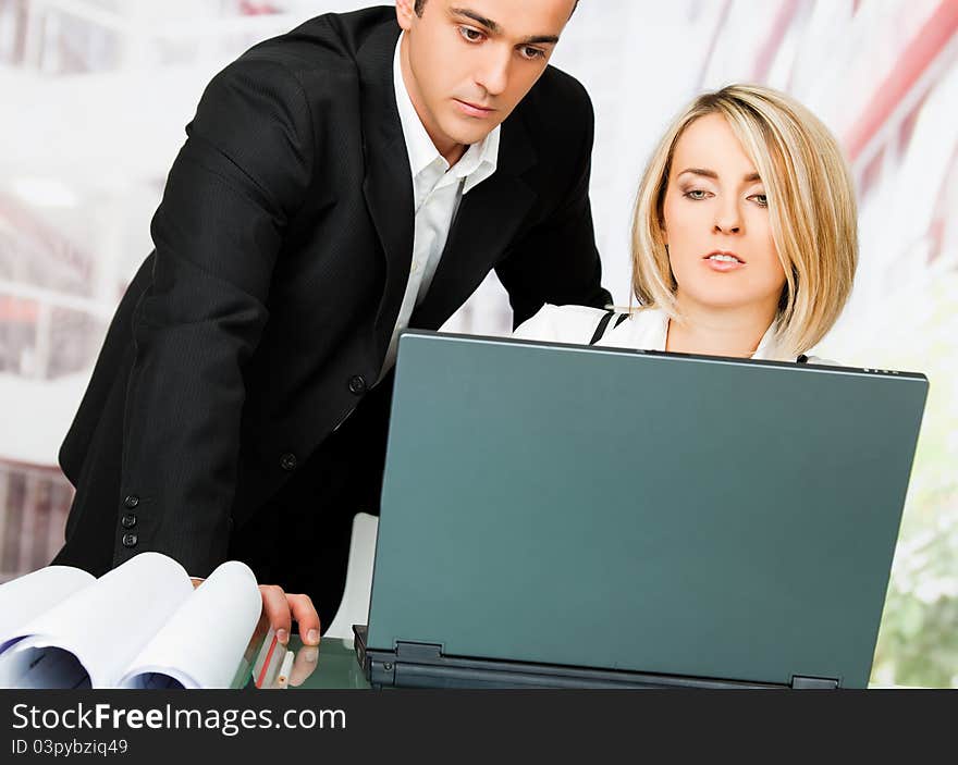 Male and female architects behind laptop and blueprints, looking serious. Male and female architects behind laptop and blueprints, looking serious