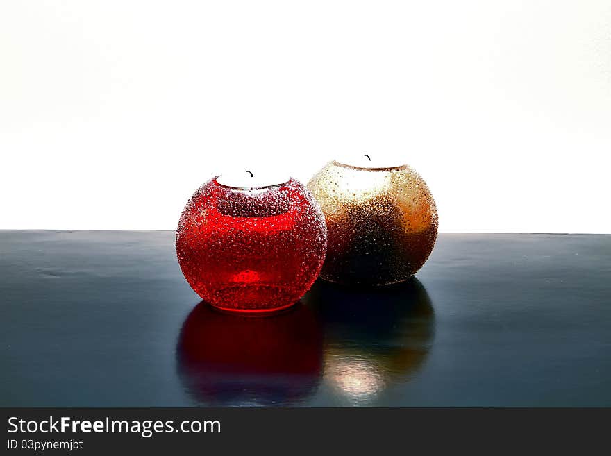 Two candles, shiny red and shiny gold, laying on black surface with white background with nice reflection on black.