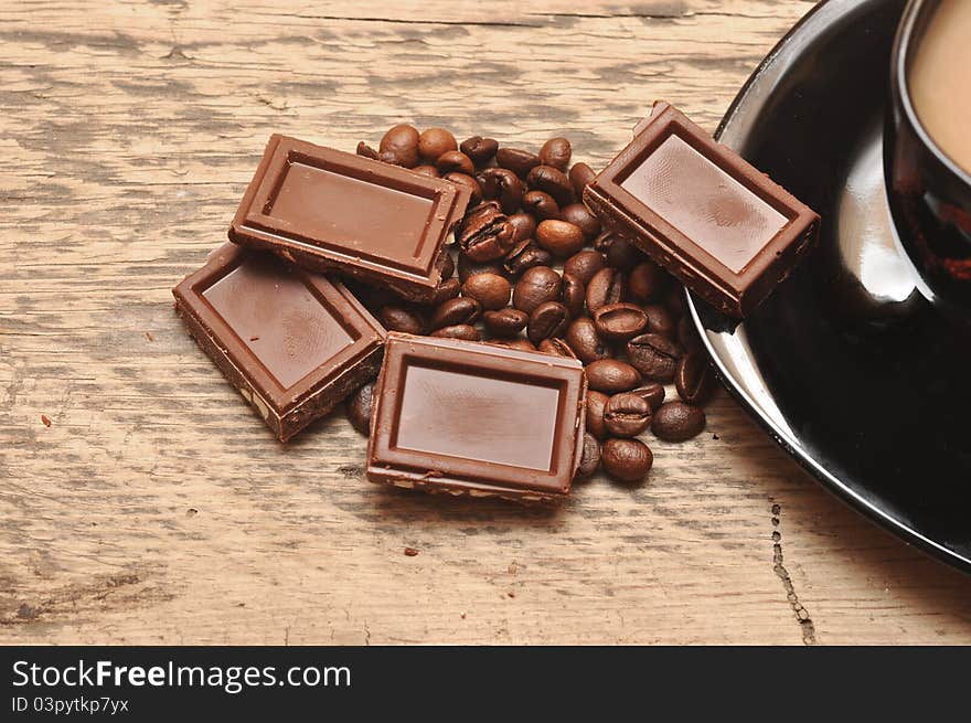 Closeup of freshly prepared cup coffee with beans and chocolate on wood background