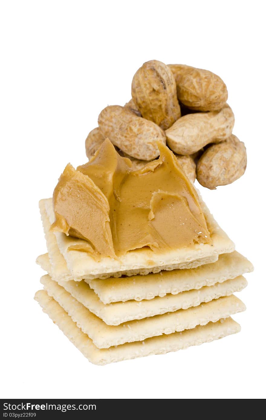 Cracker with peanut butter and peanuts in the background on white.