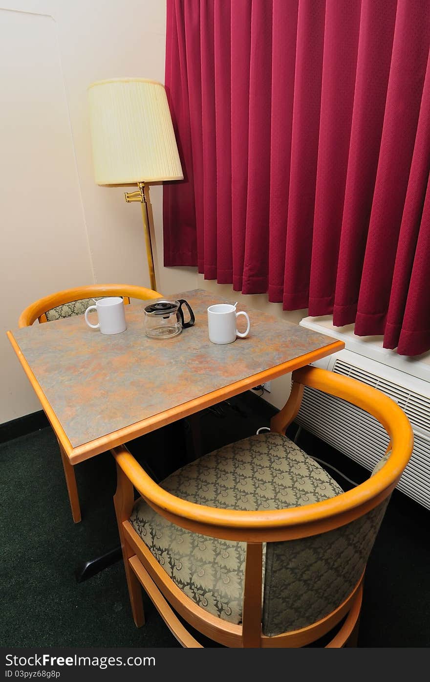 White drinking glasses on table with chairs and red curtain.