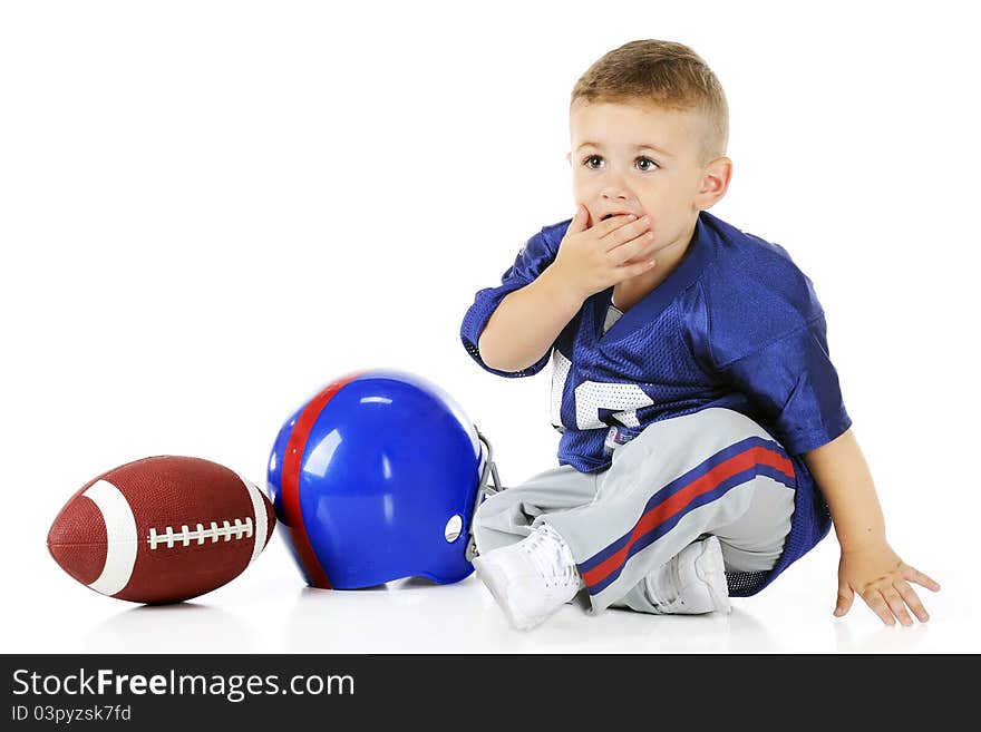 An adorable toddler in his football uniform covering his mouth in unbelief. His helmet and football sit by his side. Isolated on white. An adorable toddler in his football uniform covering his mouth in unbelief. His helmet and football sit by his side. Isolated on white.