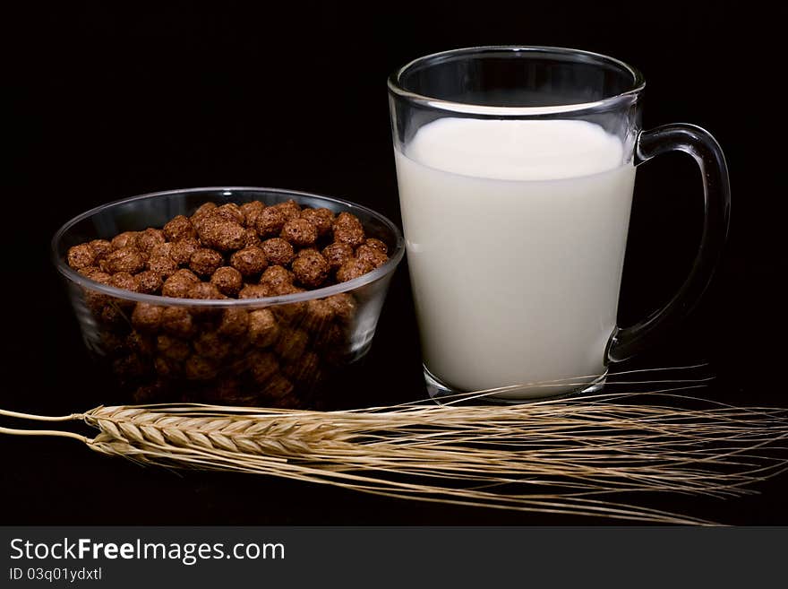 Chocolate balls, a glass of milk and wheat ears called a black background